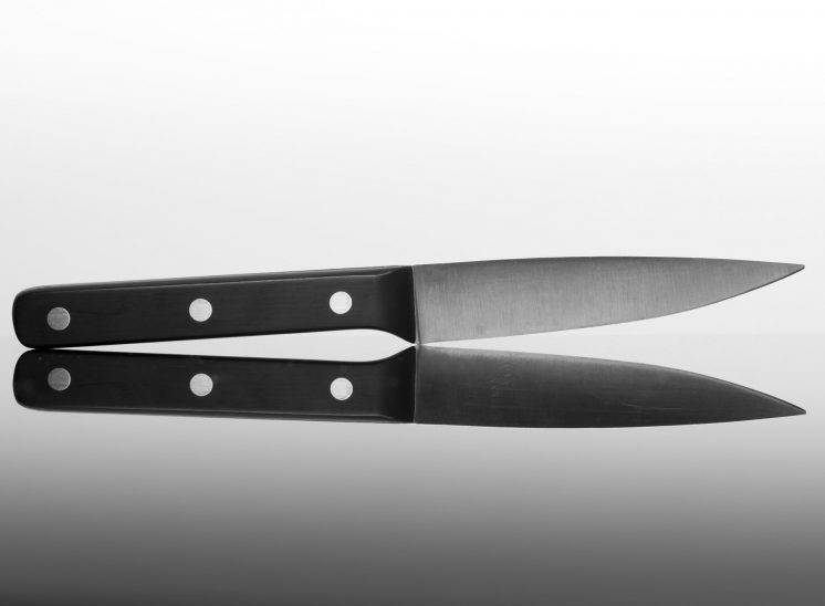 Side profile of a kitchen knife on black glass with reflection