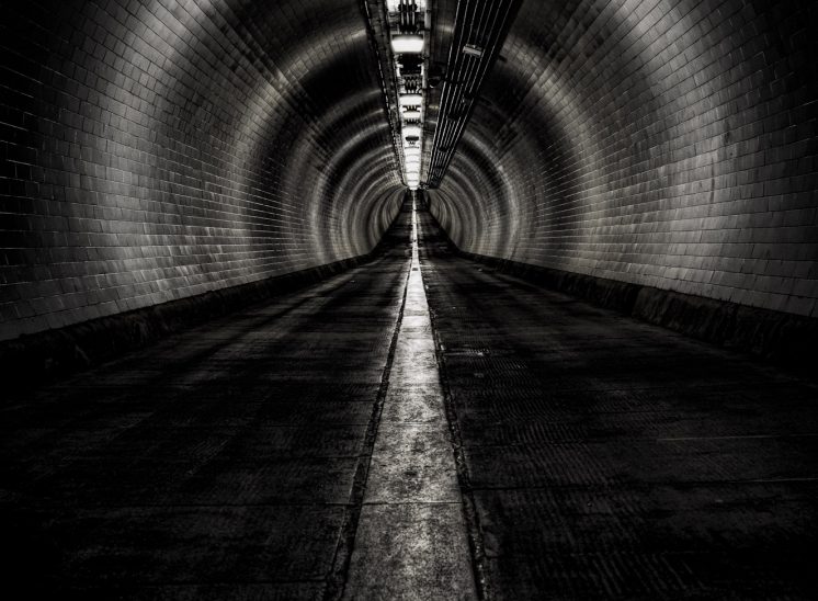 A black and white photograph taken inside the empty, brick-lined Woolwich foot tunnel underneath the River Thames, London