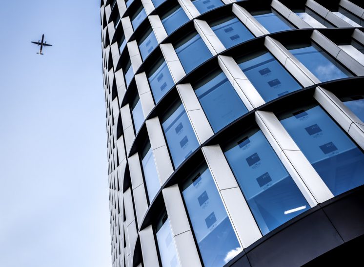 Aeroplane passing while looking up at modern glass office building in London