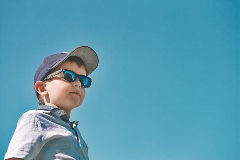 Boy wearing a cap and sunglasses with a clear blue sky background