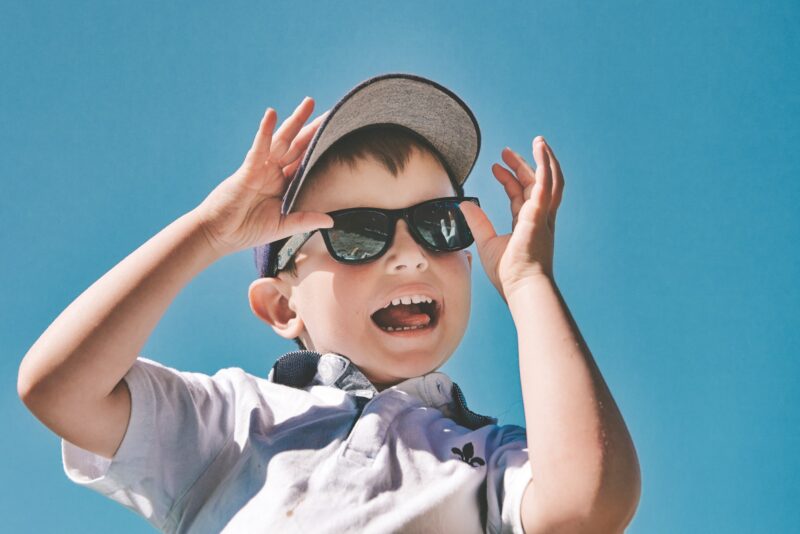 Boy messing about while wearing a cap and sunglasses with a clear blue sky background