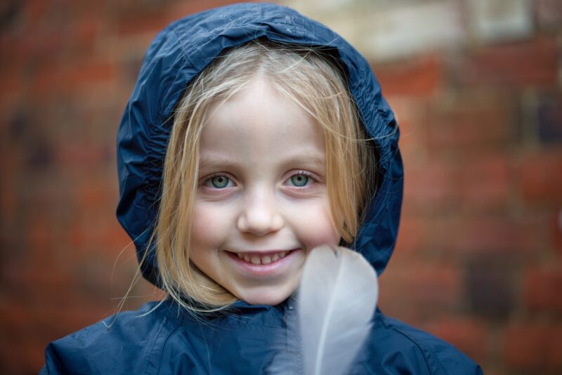 Girl in raincoat holding a feather and smiling to camera